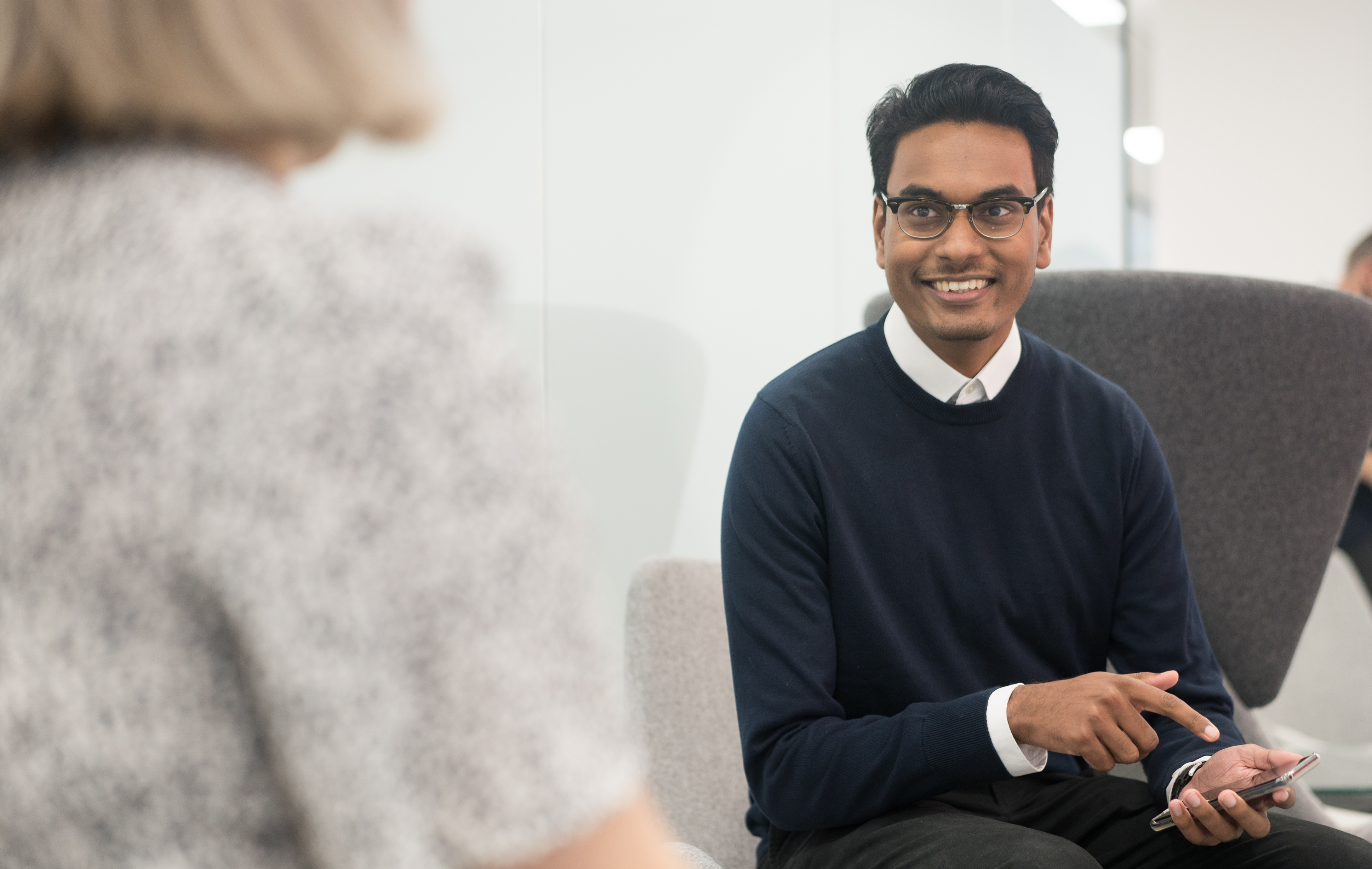A co-worker pointing at his phone as he looks at another co-worker.
