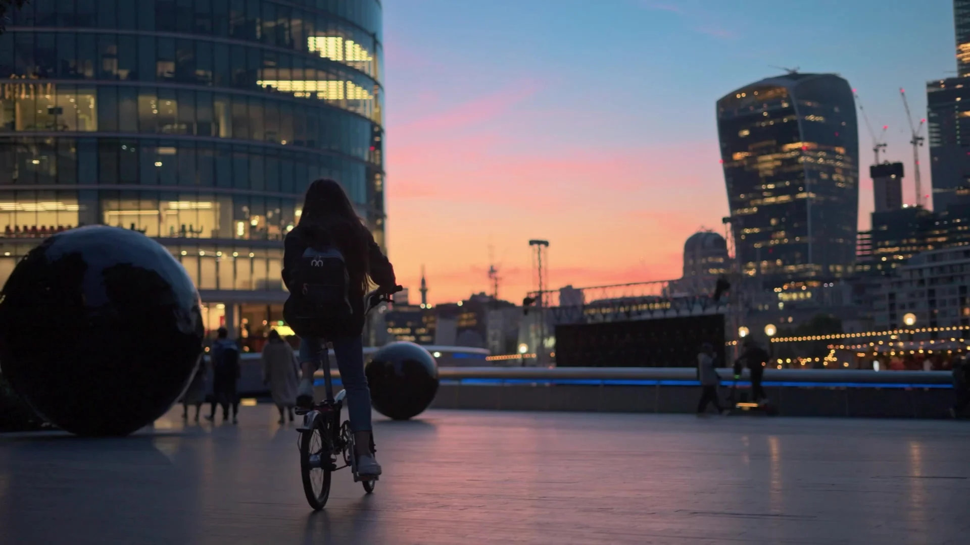 Woman on bicycle looking at a sunset through tall buildings.