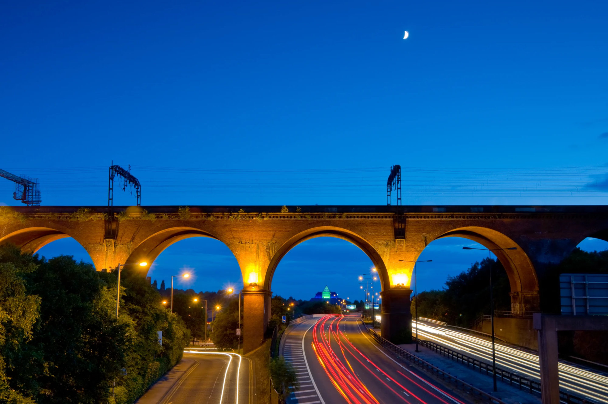 Motorway traffic passing through arches of a rail bridge at night.
