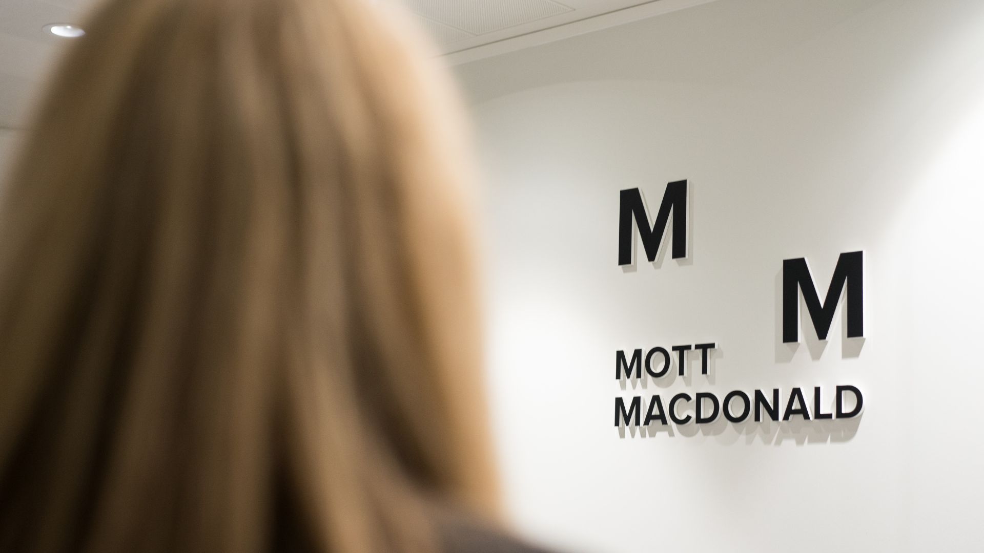 Mott MacDonald logo on a wall, with the view of a woman's head in the foreground