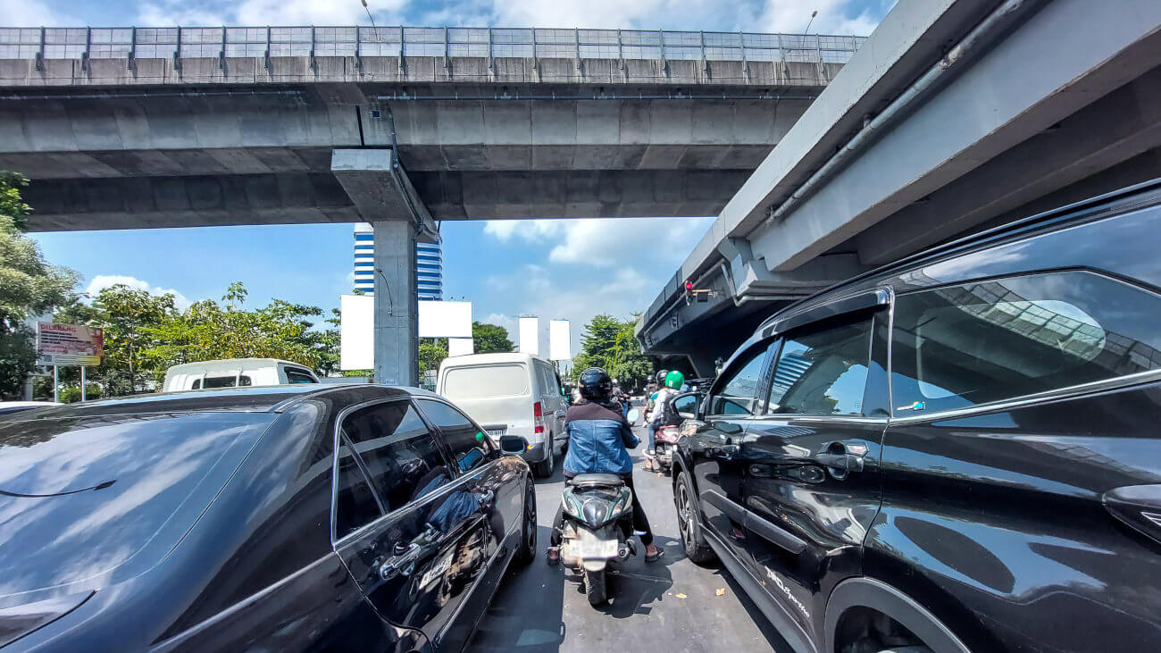 Mopeds weaving through traffic under an overpass.