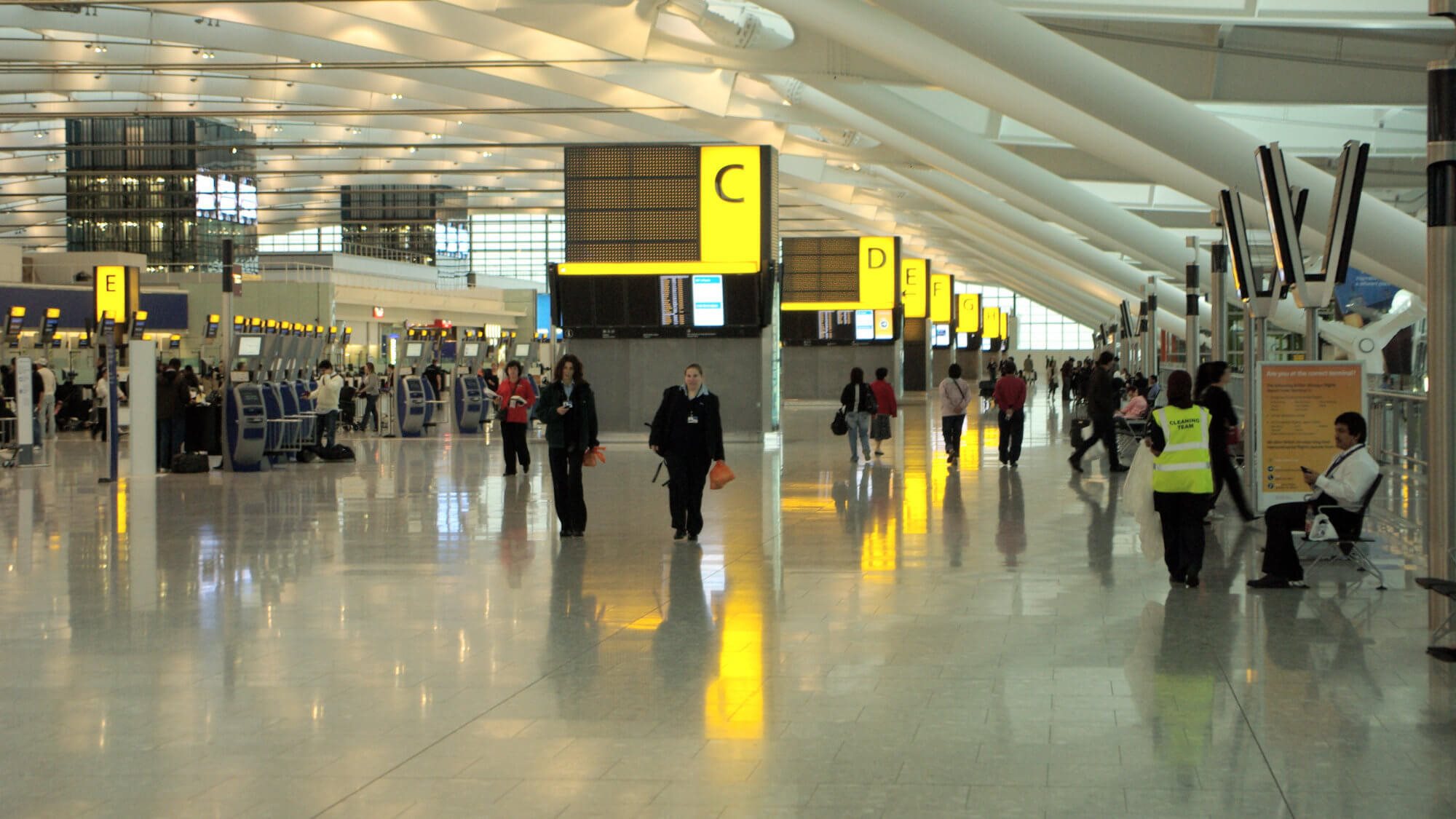People walking past check in gates at a Heathrow terminal.