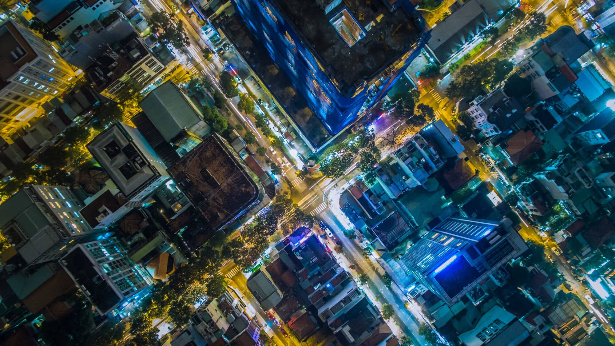 Aerial shot of illuminated city roads and buildings at night.