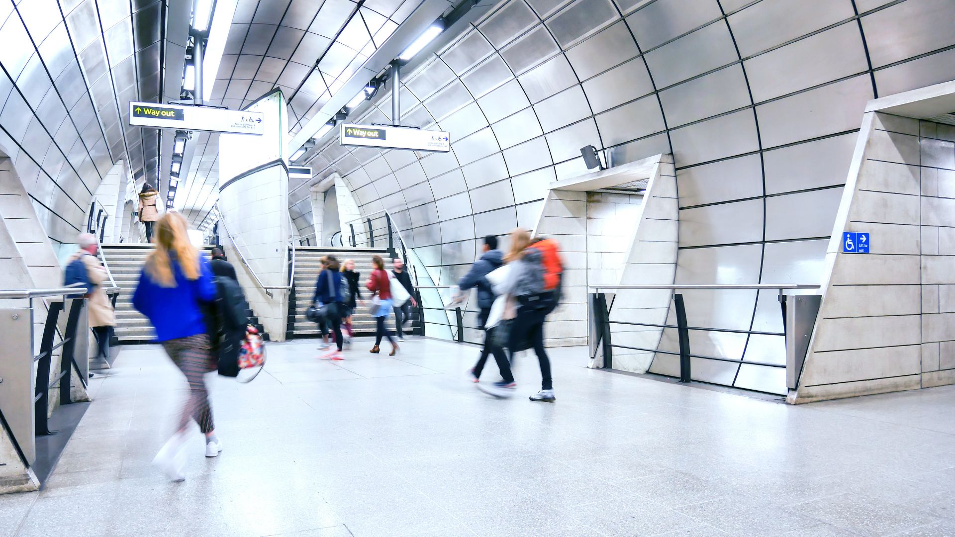 People moving through a modern London Underground station concourse, with stairs, &ldquo;Way out&rdquo; signage and platform-level architecture reflecting TfL&rsquo;s transport network.