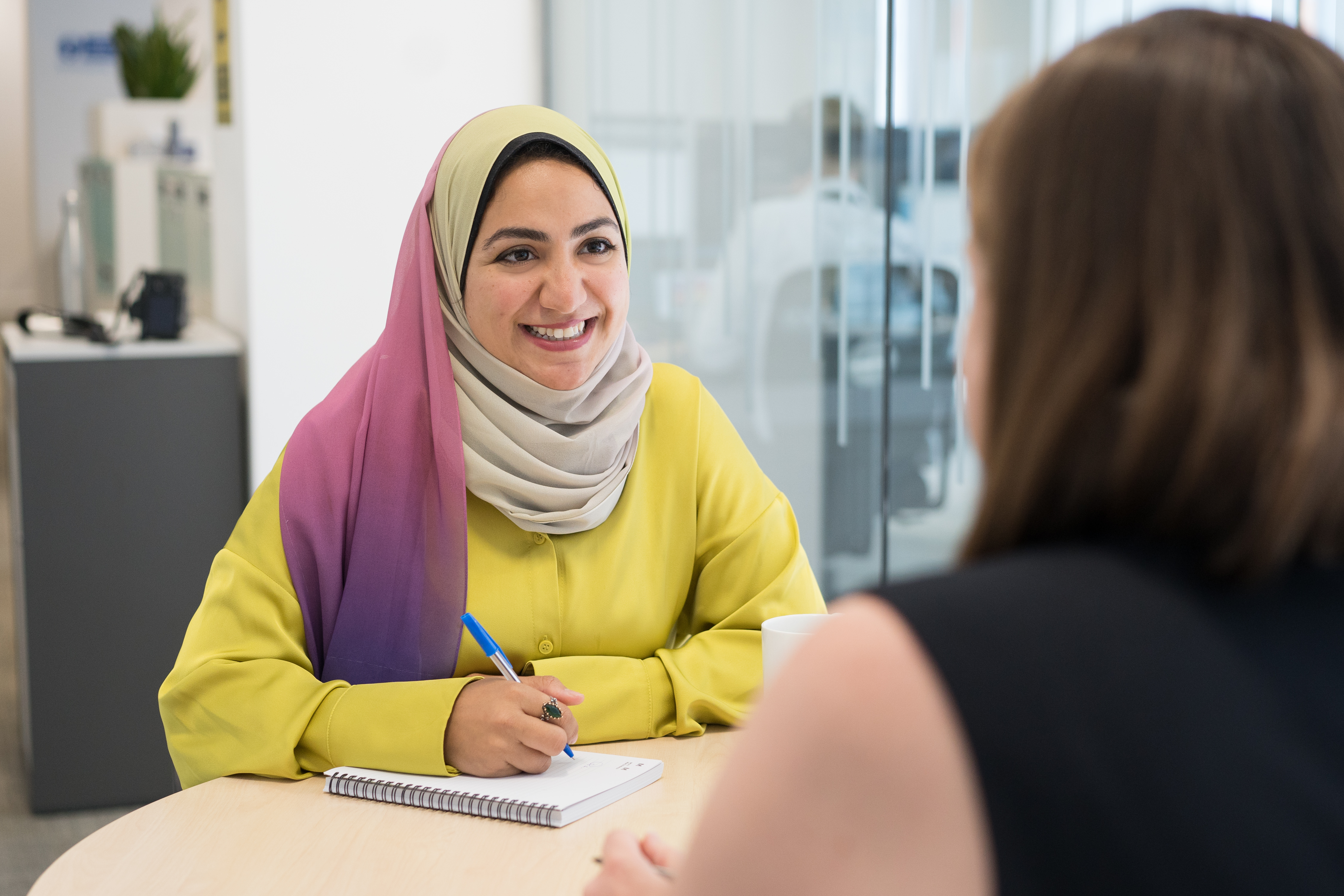 A woman sitting across the table from another woman, with one taking notes. 