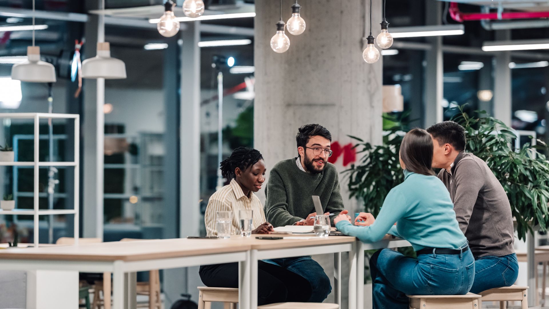 Team members gathered around a table in a modern office, discussing plans and reviewing information together during a collaborative meeting.