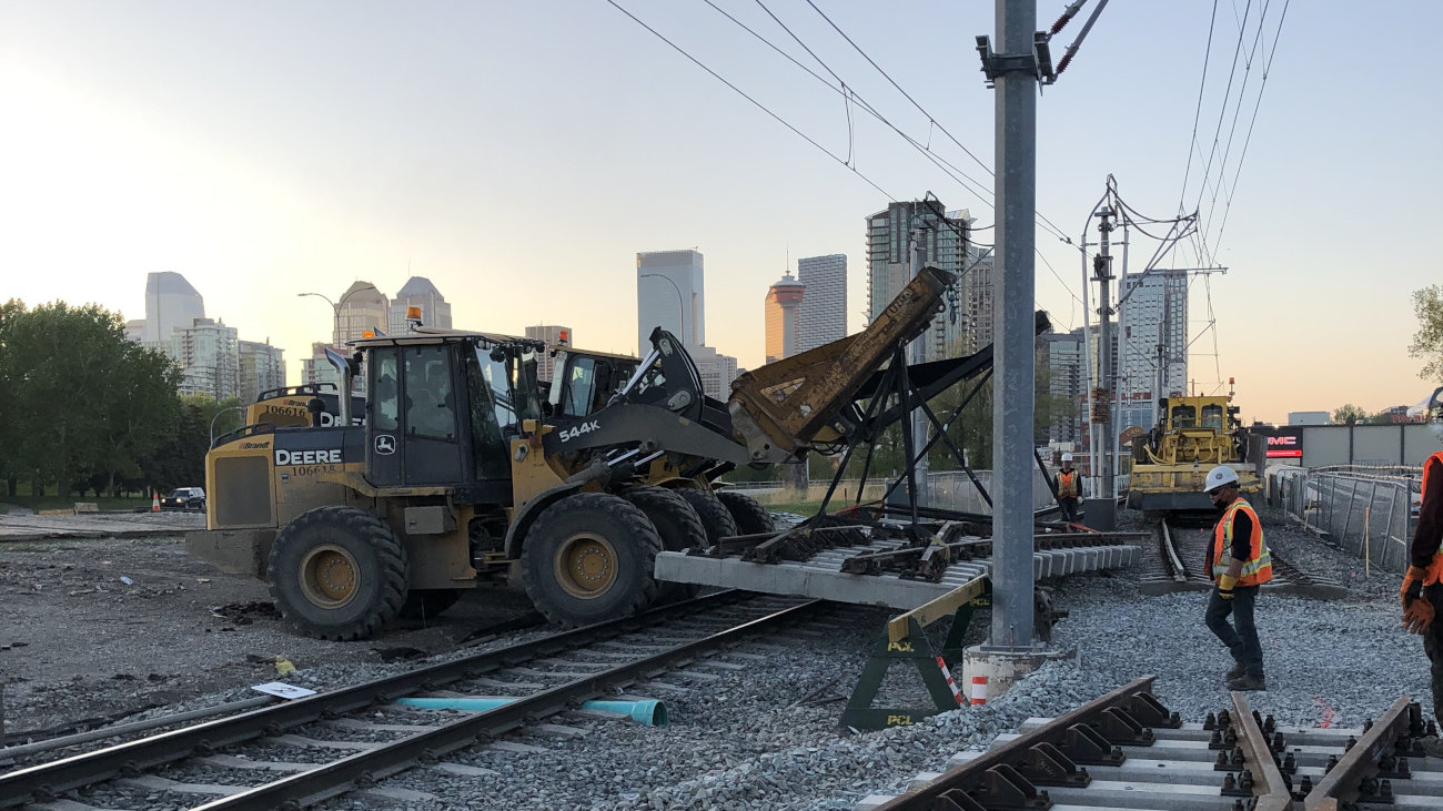 Bulldozers working on rail tracks with skyscrapers in the background.