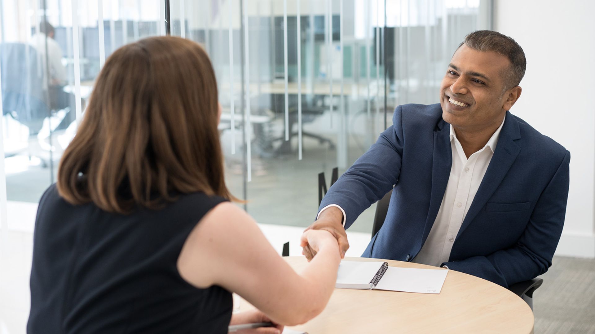 Professional meeting with two colleagues shaking hands across a desk in a modern office, representing PFI handback transition, collaboration and governance planning
