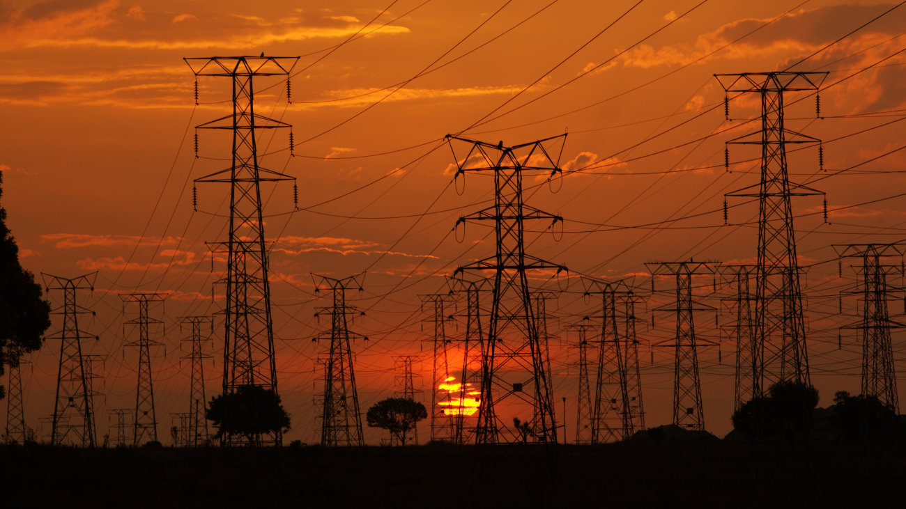 Electricity pylons with setting sun behind.