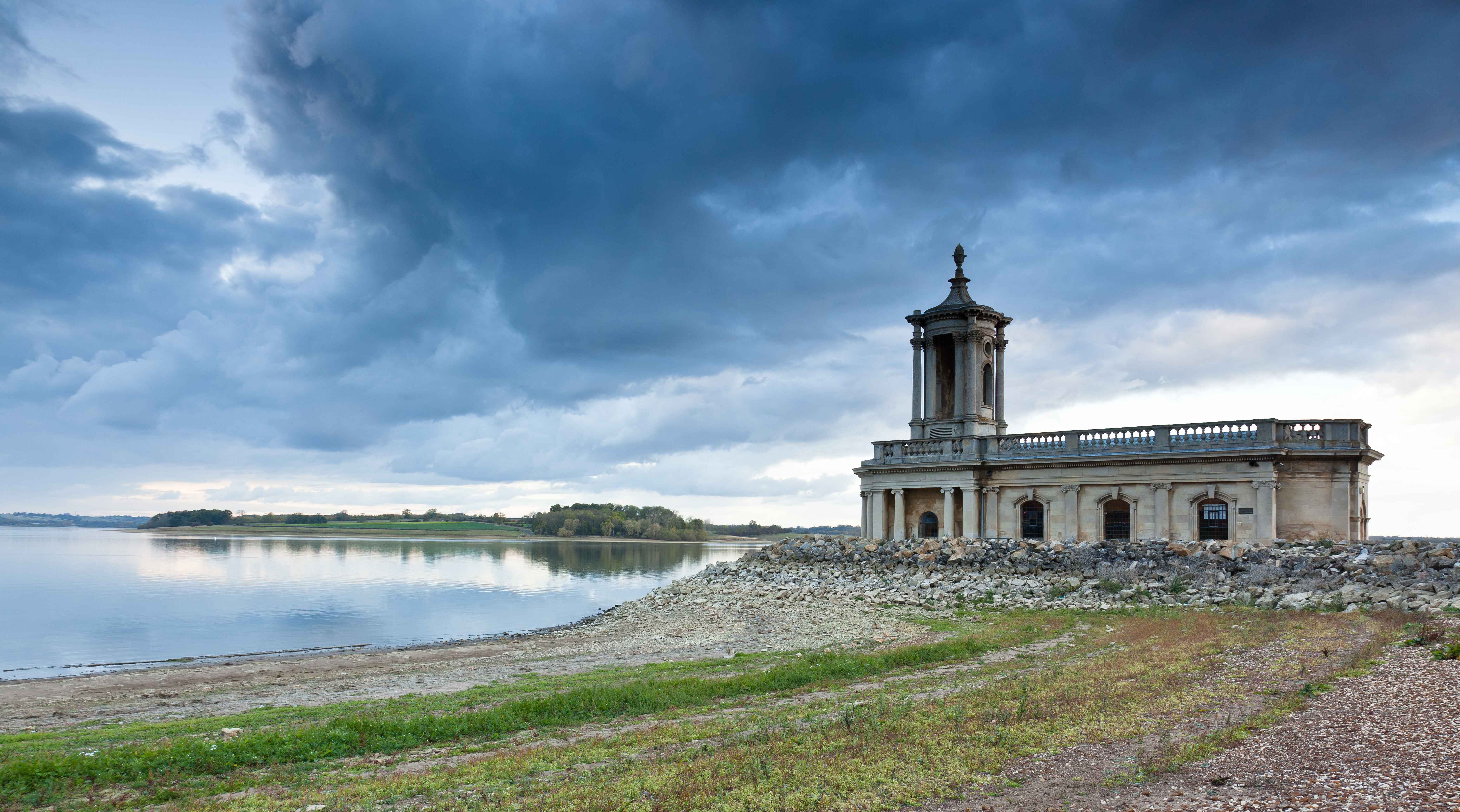 Historic waterfront building surrounded by rocky shoreline and stormy skies.