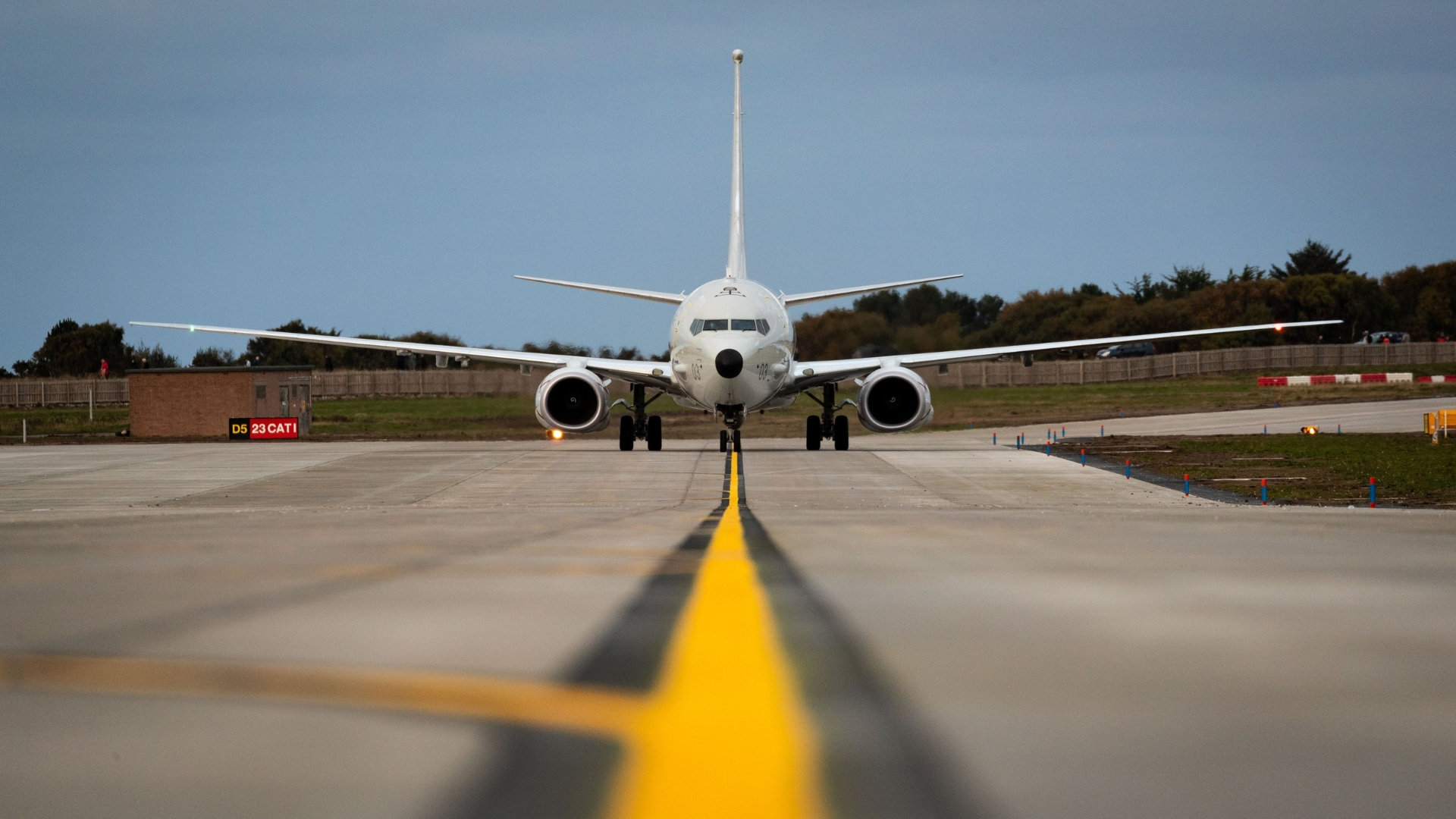 A P‑8A Poseidon aircraft facing directly toward the camera on a runway at RAF Lossiemouth, with a bright yellow line marking visible on the tarmac in front of the nose.