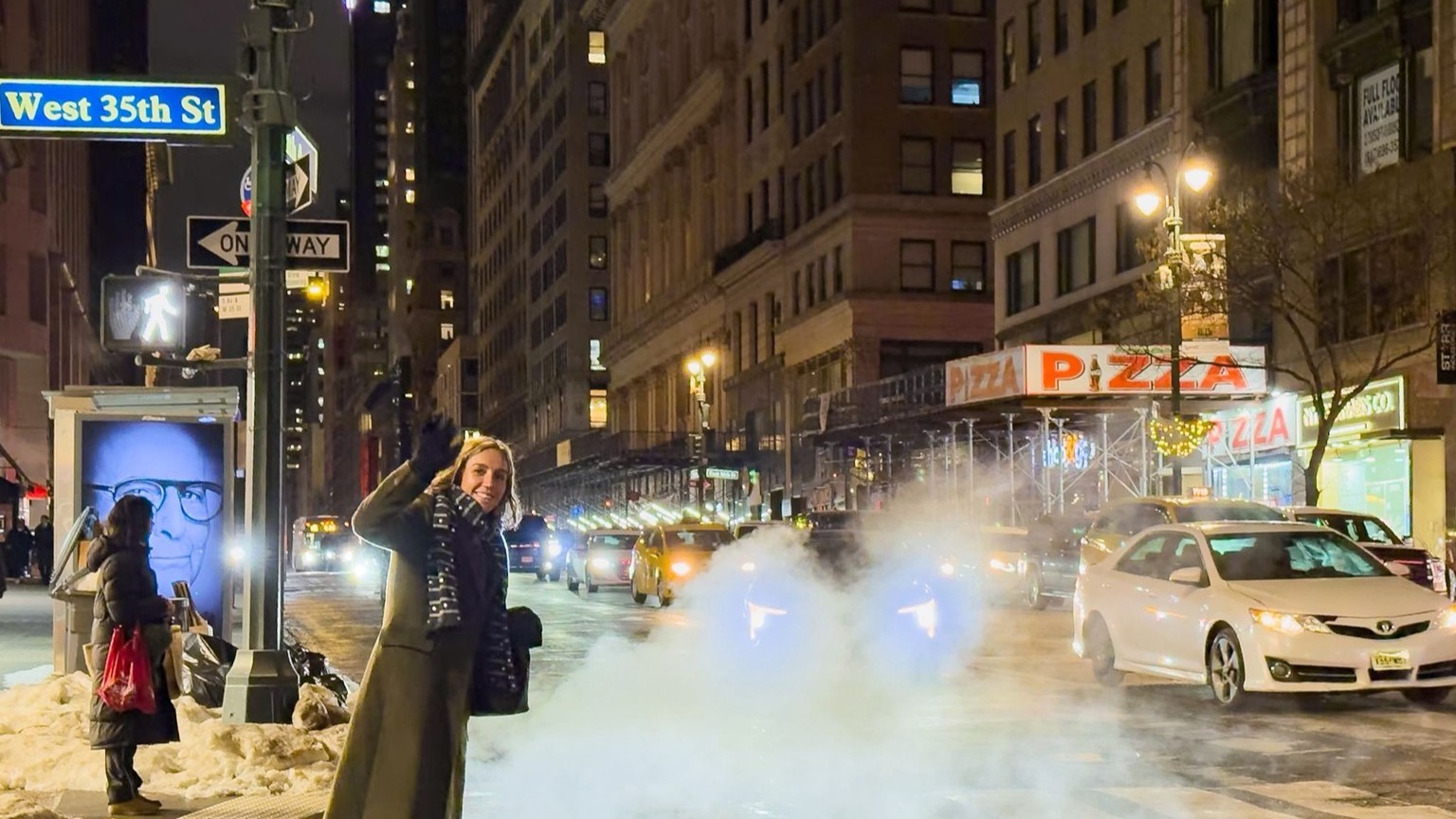 Night-time street scene on West 35th St, New York, with a person waving at the curb as city traffic passes, steam rising from the road, illuminated by streetlights and a pizza shop sign.