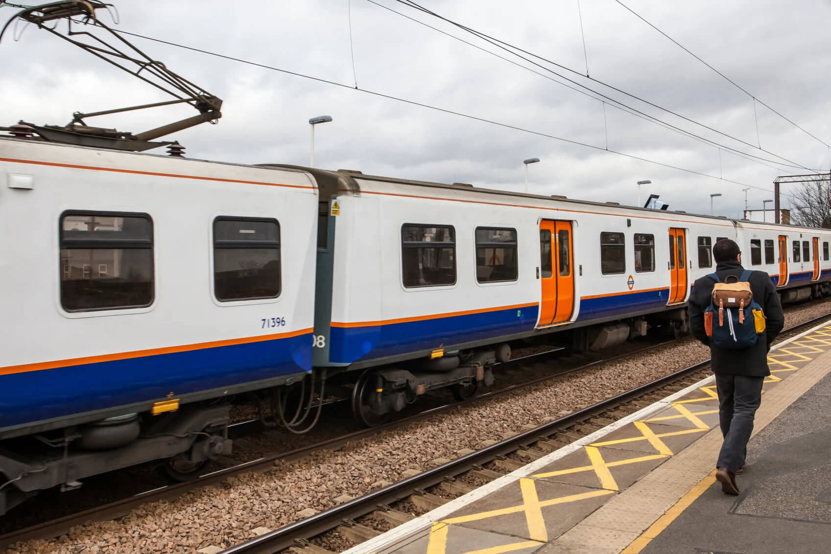 Man walking past a train along a London Overground platform.