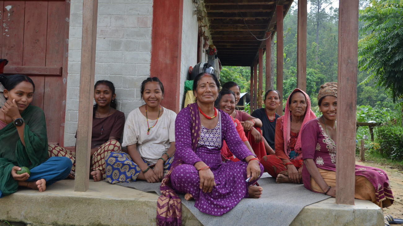 Group of women sitting under a veranda.