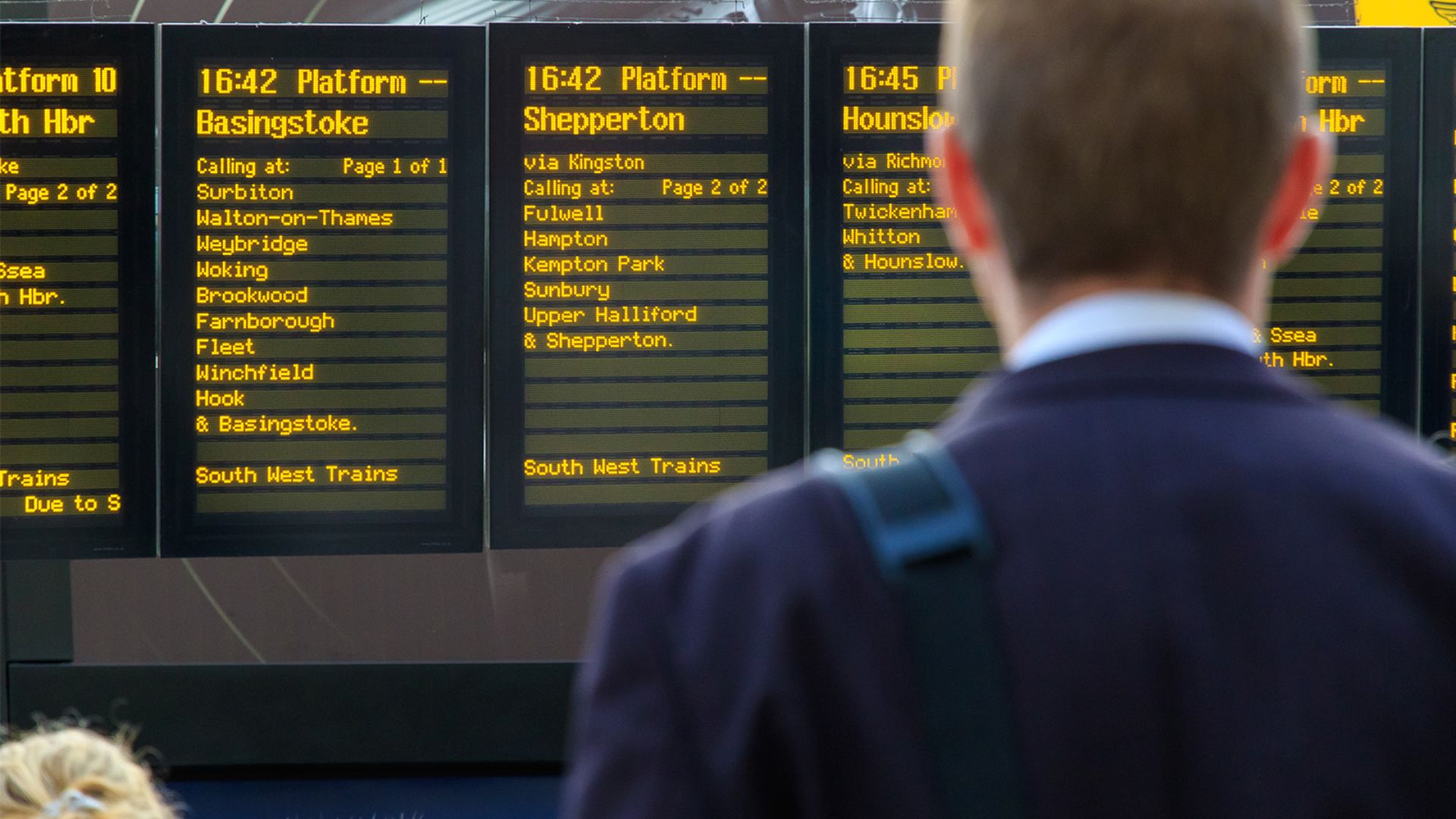 Passenger viewing live departure boards at a railway station, highlighting the role of information, passenger experience and operational safety in Great Britain&rsquo;s rail network.