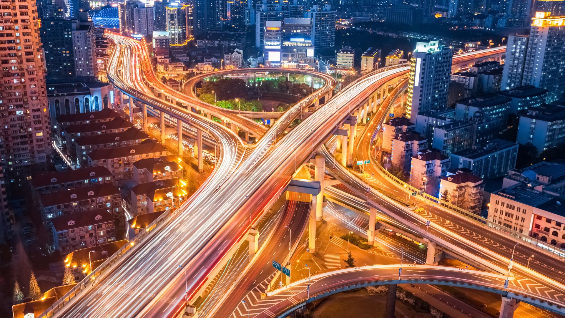 Aerial night view of a complex urban road interchange with fast‑moving traffic, representing transport networks and data‑driven mobility.