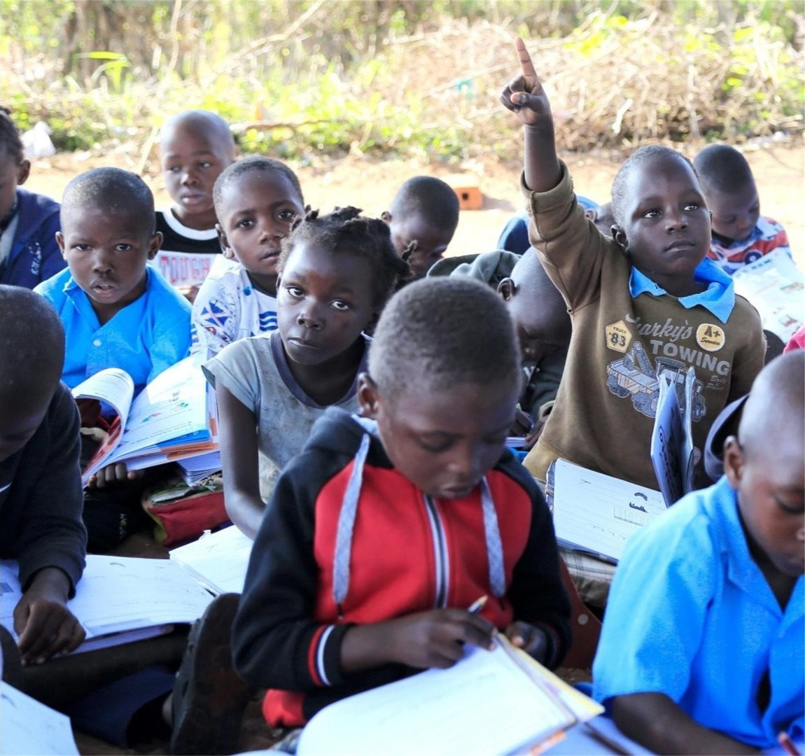 Young children sat on the floor holding textbooks.
