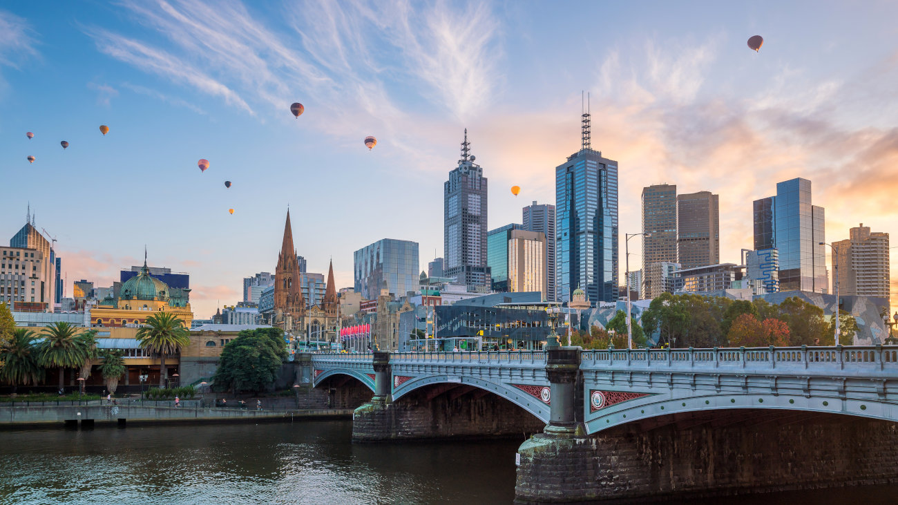 Hot air balloons floating over skyscrapers and a river.