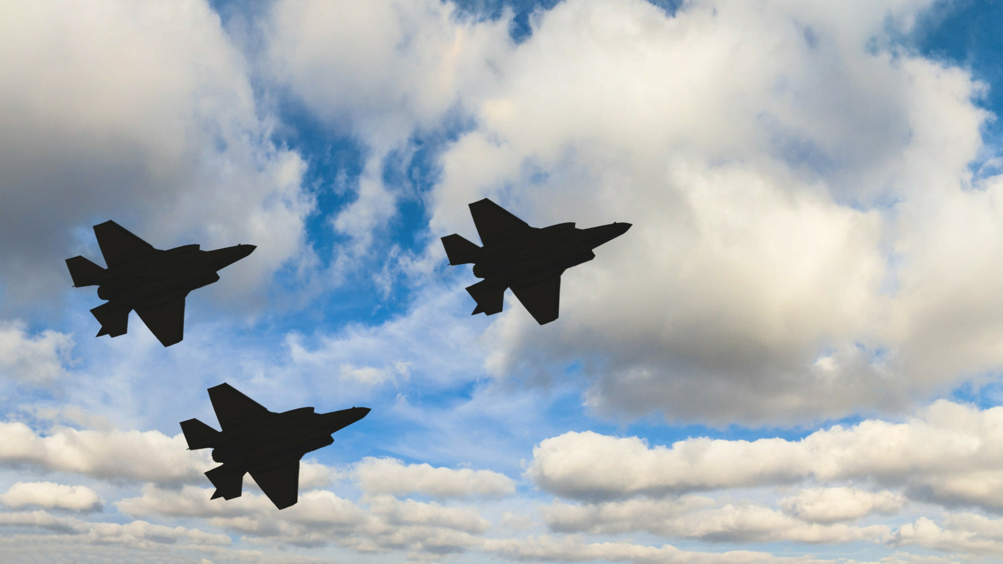 Three F-35 fighter jets flying under clouds.