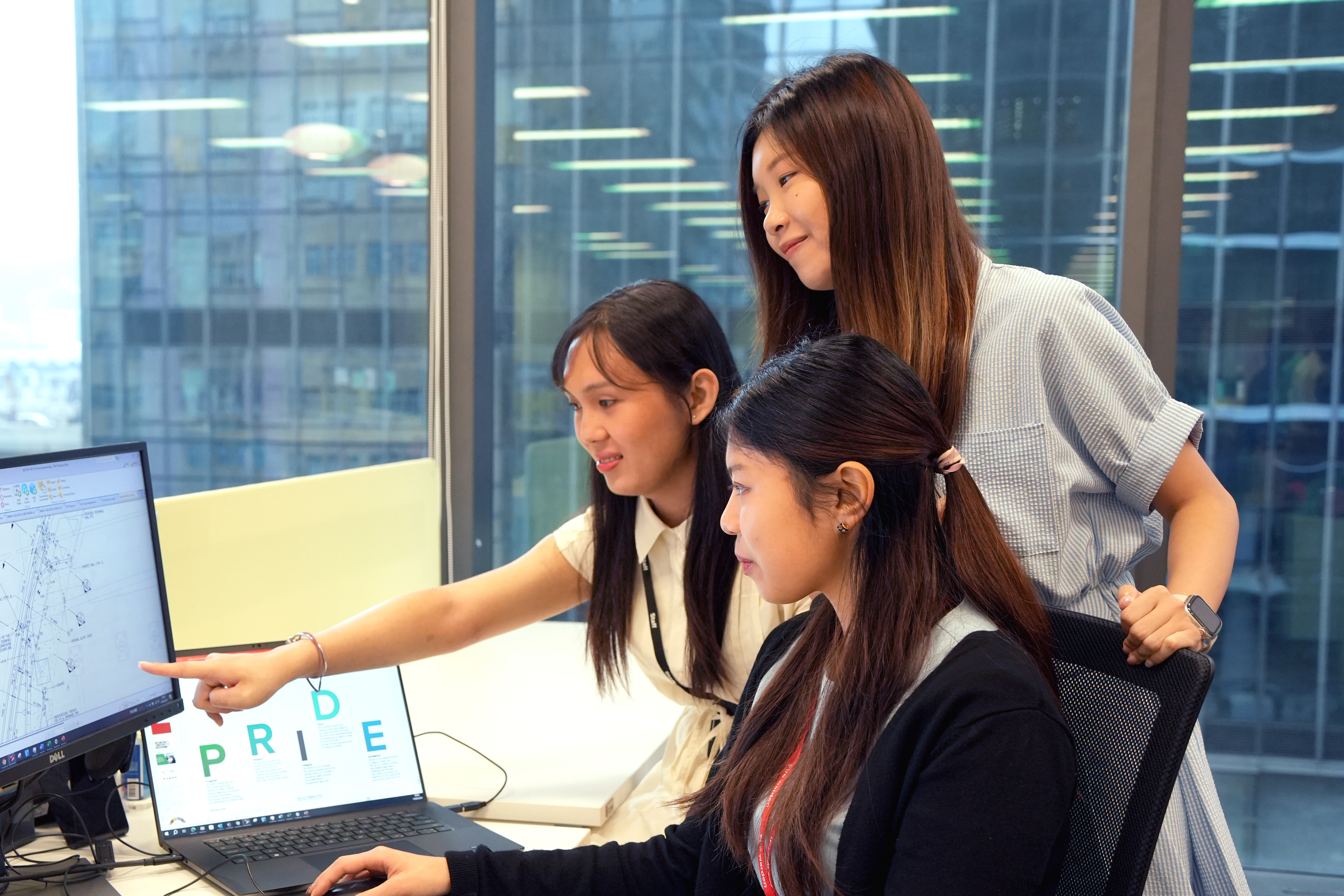 Three co-workers looking at a desktop monitor in an office.