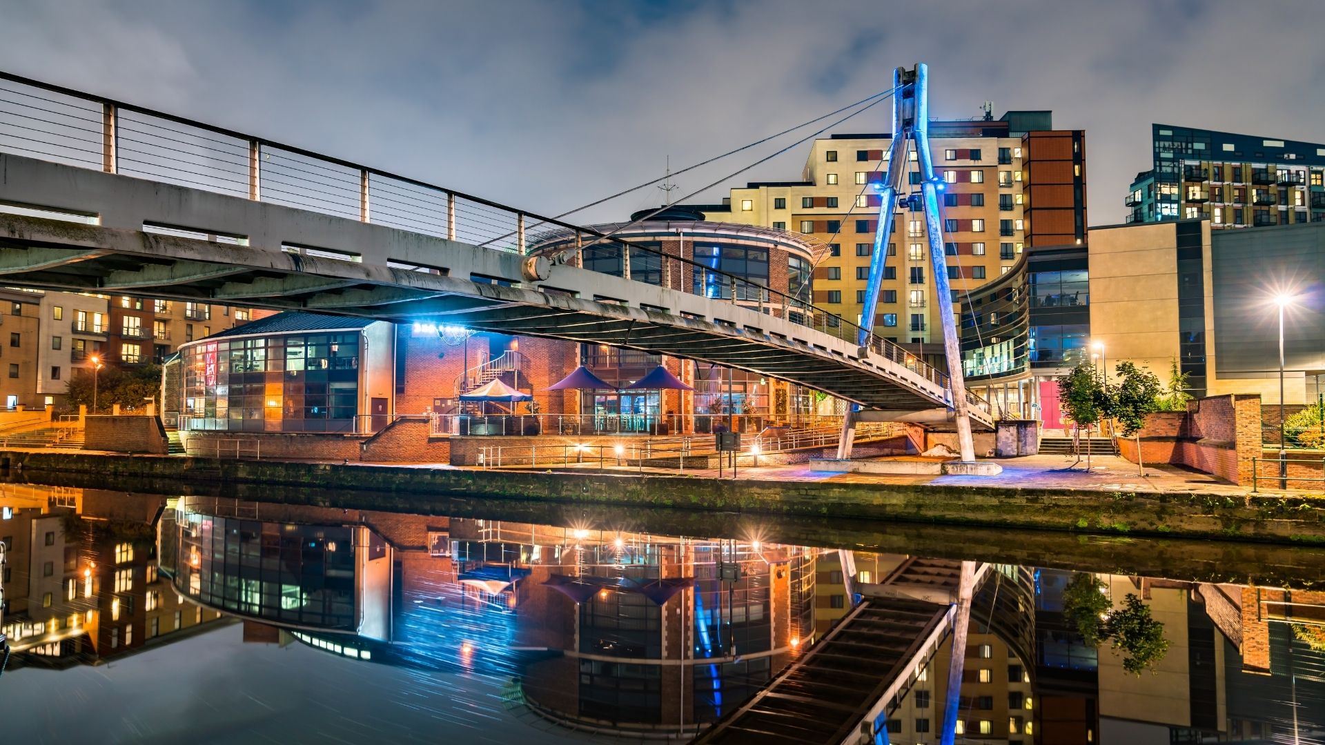 Modern pedestrian footbridge over Leeds waterfront at night, with illuminated residential buildings and canal reflections, representing urban regeneration and place-based infrastructure development
