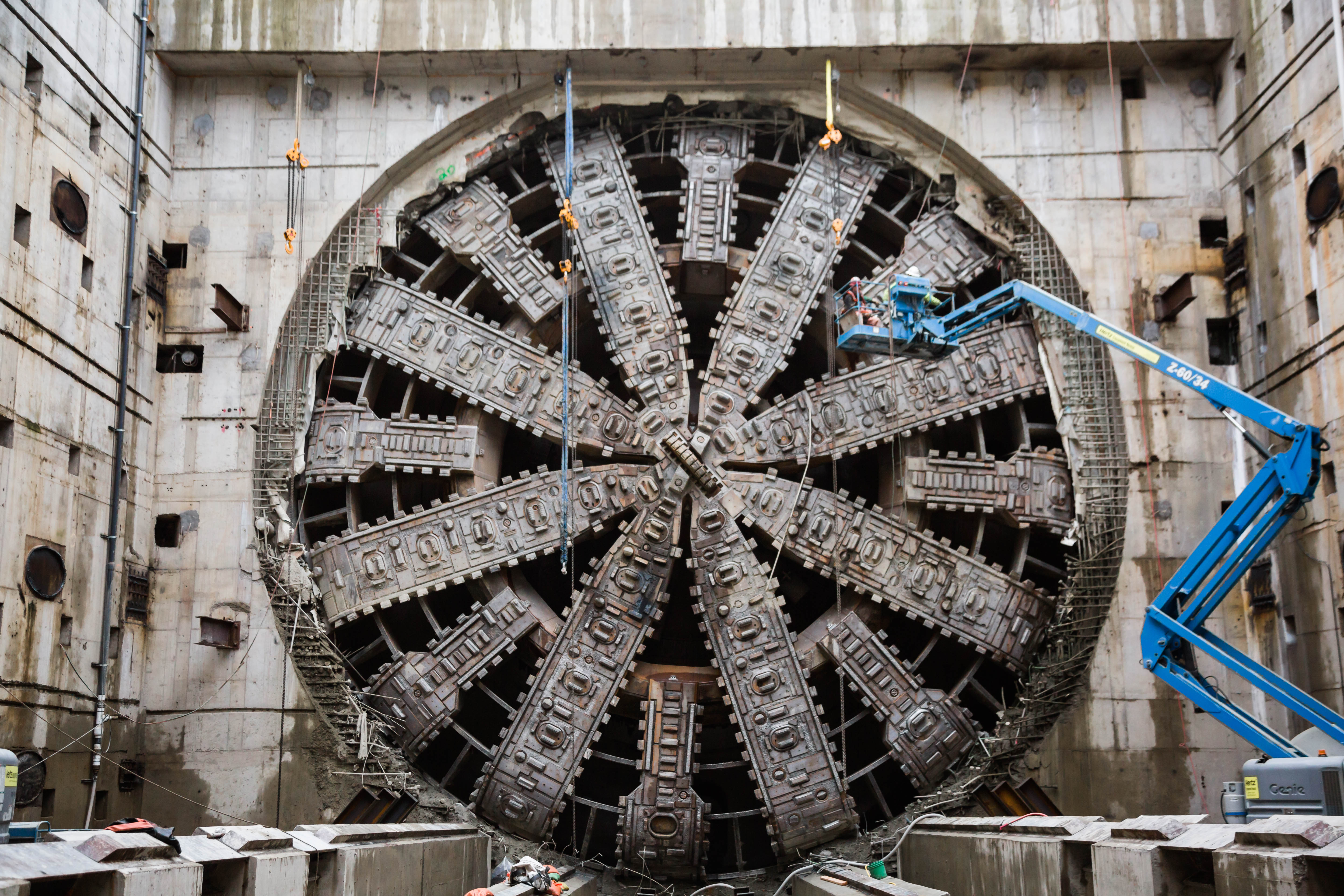 A blue construction crane hovers outside of a massive viaduct tunnel in Alaska. 