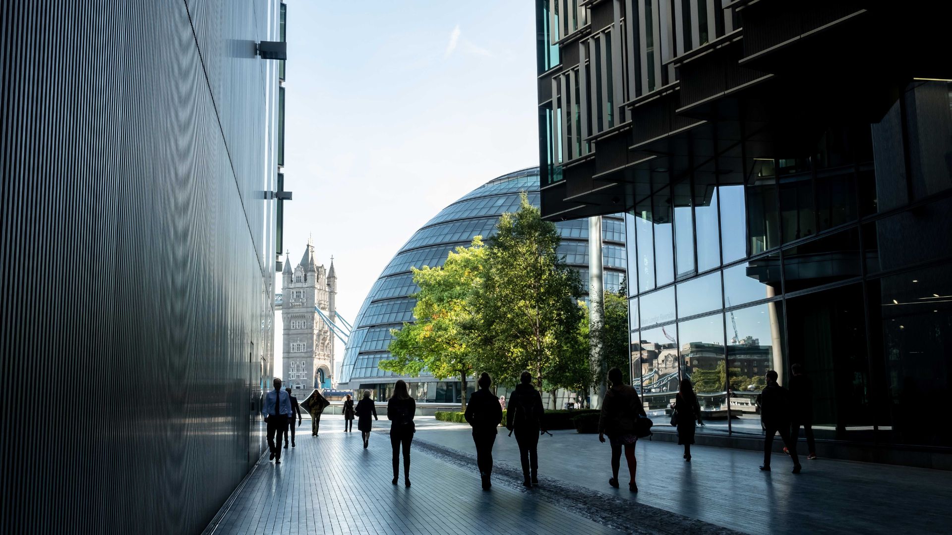 An urban pedestrian walkway framed by contemporary buildings, with trees and iconic London landmarks visible, illustrating the intersection of city life, infrastructure, and sustainable place-based planning.