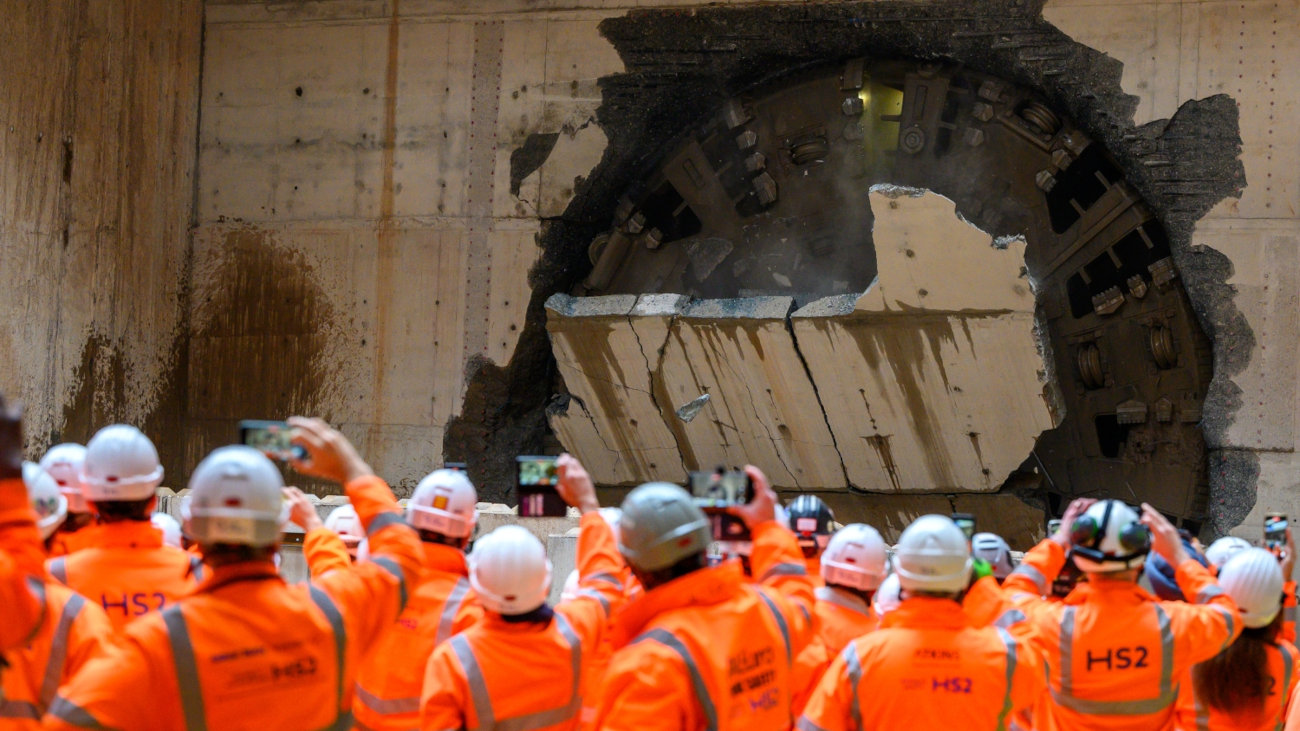 Construction workers in safety gear raise phones to document HS2’s 23-mile deep bore tunnelling milestone, supported by Mott MacDonald.