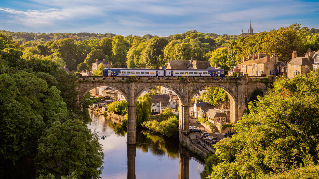 A train crossing a bridge over a river with houses and a church in the background.
